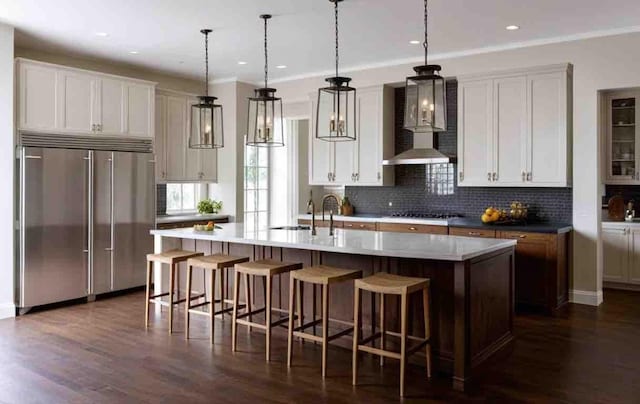 kitchen with white cabinetry, built in refrigerator, hanging light fixtures, a large island, and wall chimney range hood