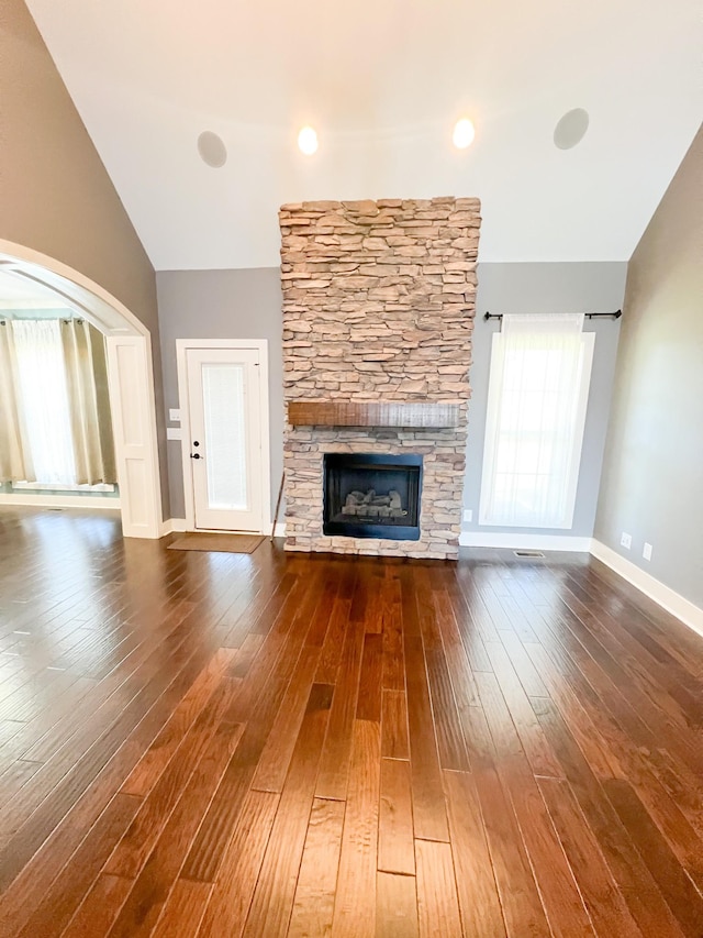 unfurnished living room featuring plenty of natural light, dark wood-type flooring, and a stone fireplace