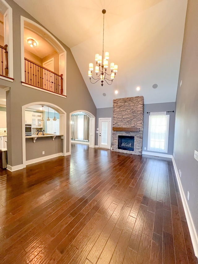 unfurnished living room with high vaulted ceiling, a fireplace, a chandelier, and dark wood-type flooring