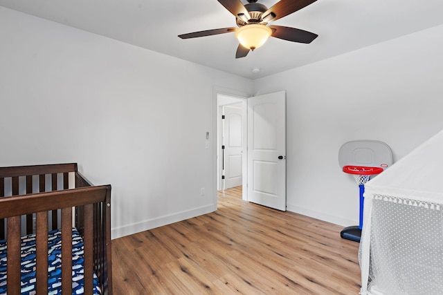 bedroom with a nursery area, ceiling fan, and light wood-type flooring