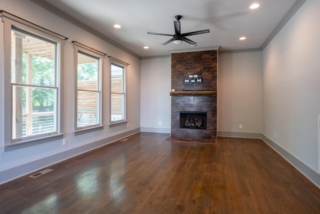 unfurnished living room featuring a tiled fireplace, ceiling fan, crown molding, and dark wood-type flooring