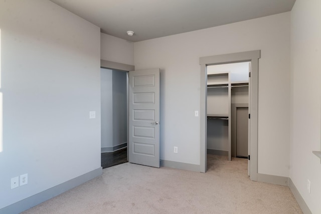 unfurnished bedroom featuring baseboards, a closet, a walk in closet, and light colored carpet