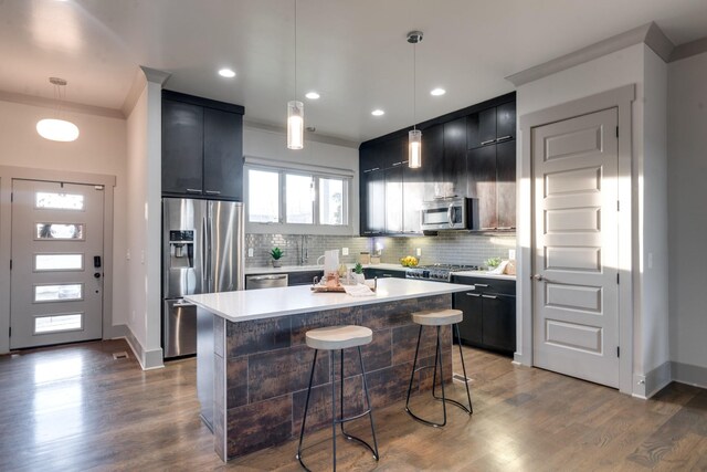 kitchen featuring a kitchen breakfast bar, stainless steel appliances, dark cabinetry, light countertops, and backsplash