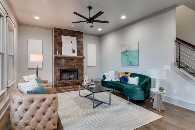 living area featuring stairs, a stone fireplace, wood finished floors, and crown molding