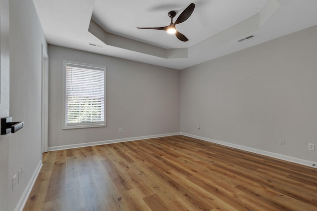 unfurnished room featuring ceiling fan, light wood-type flooring, and a tray ceiling