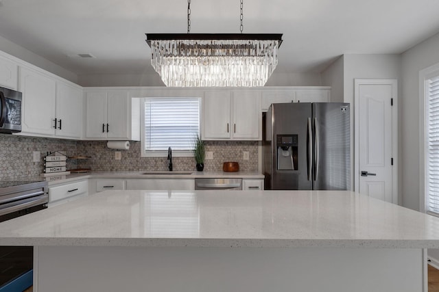 kitchen with stainless steel appliances, sink, a center island, white cabinetry, and hanging light fixtures