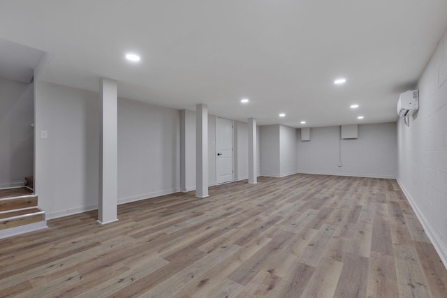 basement with a wall unit AC and light hardwood / wood-style flooring