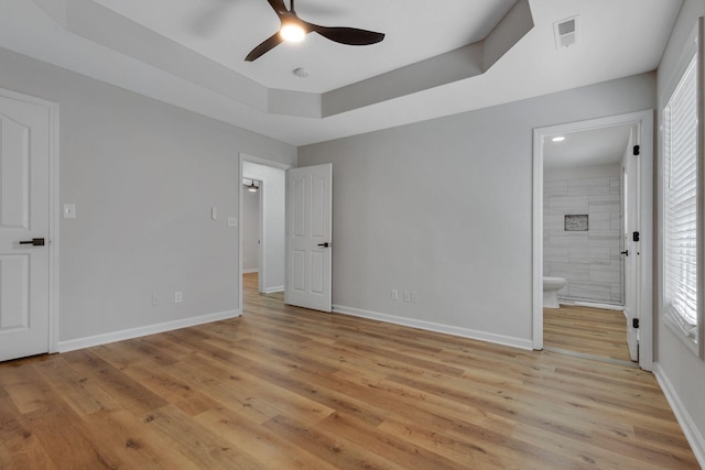 unfurnished bedroom featuring ceiling fan, light wood-type flooring, ensuite bath, and a tray ceiling