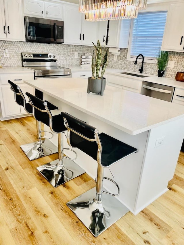 kitchen with stainless steel appliances, sink, white cabinets, light wood-type flooring, and a breakfast bar area