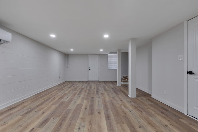 basement with a wall mounted AC and light hardwood / wood-style flooring