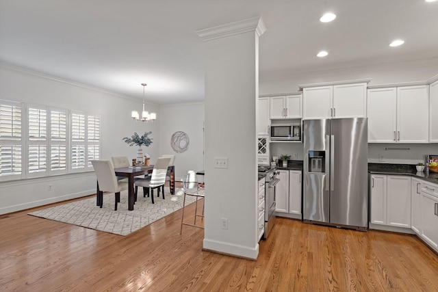 kitchen featuring stainless steel appliances, white cabinetry, hanging light fixtures, and crown molding