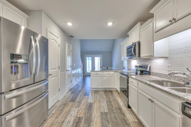 kitchen with sink, white cabinetry, stainless steel appliances, light stone counters, and kitchen peninsula