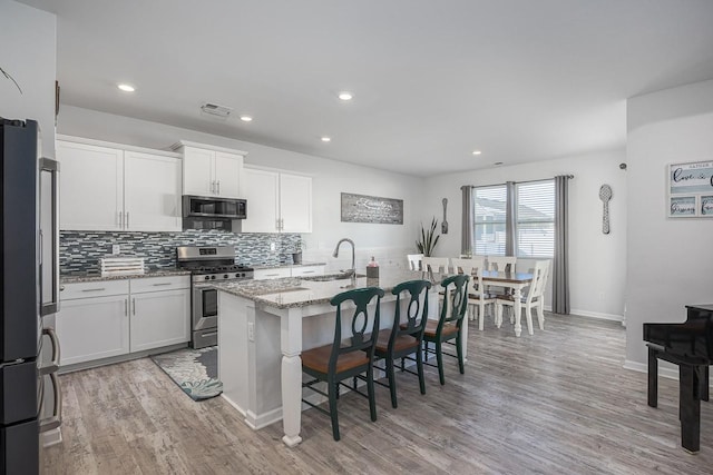 kitchen with light stone countertops, white cabinets, appliances with stainless steel finishes, an island with sink, and sink