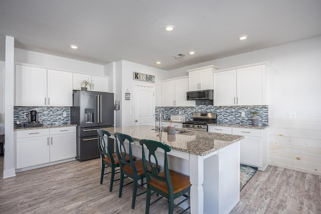 kitchen featuring white cabinets, stainless steel appliances, and a center island with sink