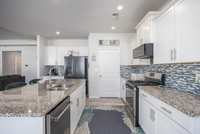 kitchen featuring appliances with stainless steel finishes, white cabinetry, decorative backsplash, sink, and a center island with sink