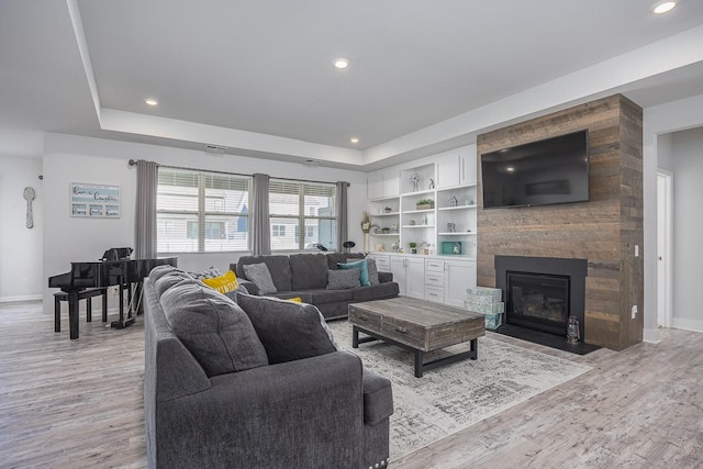 living room with a fireplace, light hardwood / wood-style flooring, and a tray ceiling