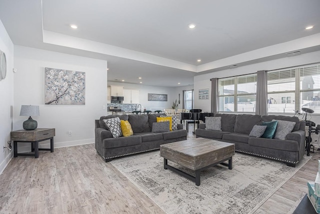 living room with light hardwood / wood-style floors and a tray ceiling