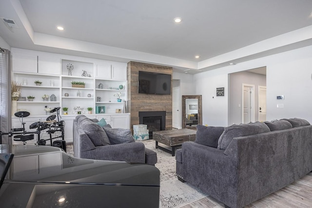 living room featuring a raised ceiling, a fireplace, and light hardwood / wood-style flooring