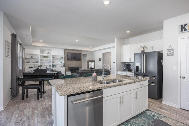 kitchen with appliances with stainless steel finishes, white cabinetry, sink, a large fireplace, and a kitchen island with sink