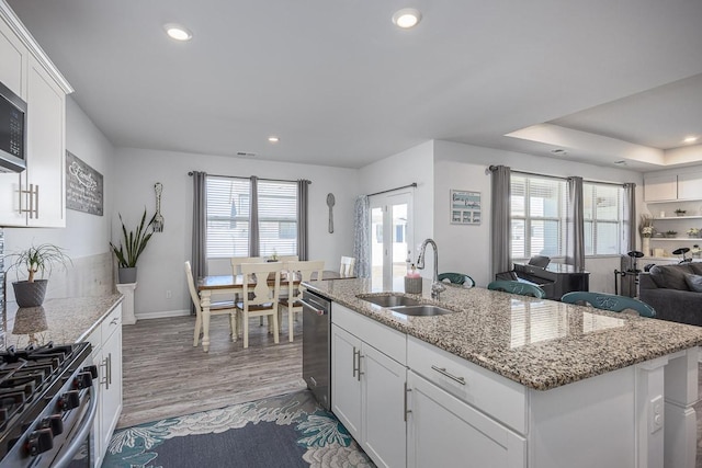 kitchen with white cabinets, a kitchen island with sink, sink, and light stone counters