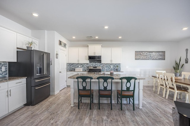 kitchen with stone counters, white cabinetry, an island with sink, and black appliances