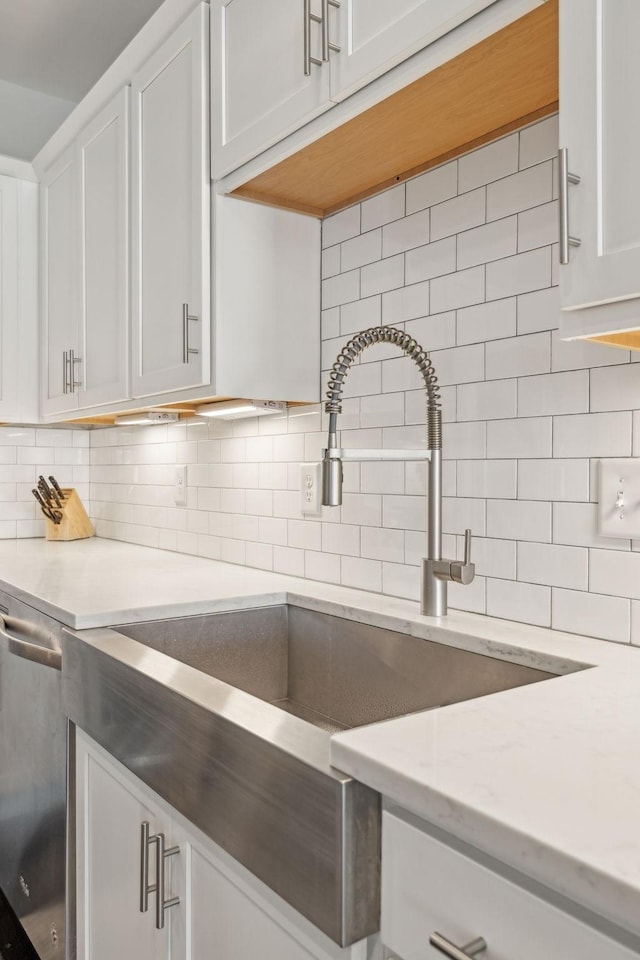 kitchen with backsplash, dishwasher, sink, white cabinetry, and light stone counters