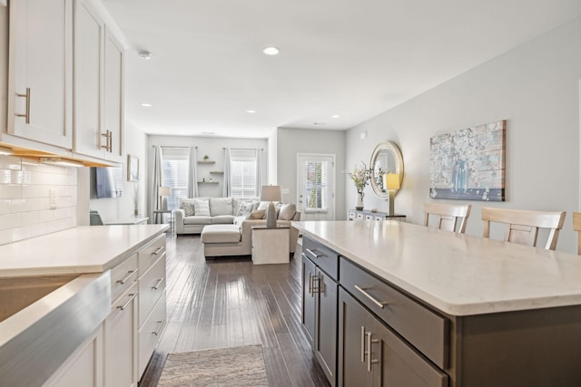 kitchen with dark hardwood / wood-style floors, a center island, a breakfast bar, decorative backsplash, and white cabinets