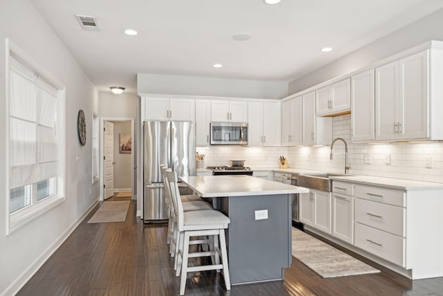 kitchen with appliances with stainless steel finishes, a kitchen island, white cabinetry, sink, and a kitchen breakfast bar