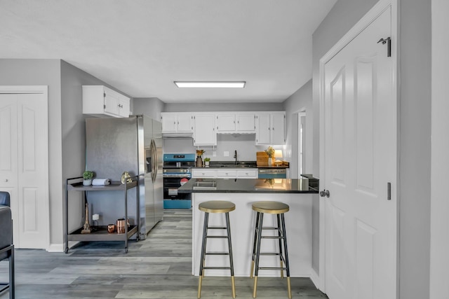 kitchen with stove, stainless steel refrigerator with ice dispenser, white cabinetry, and a kitchen bar