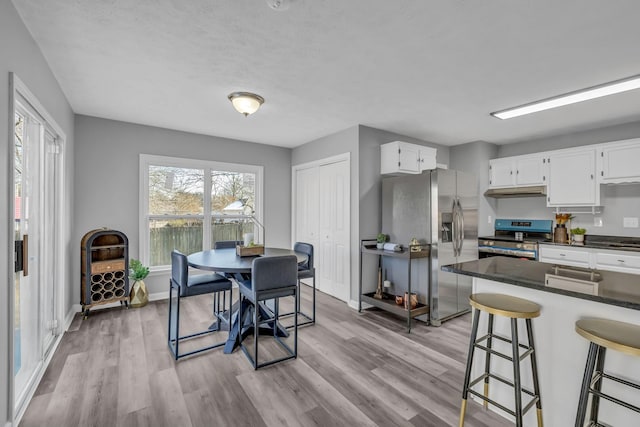 kitchen with a kitchen breakfast bar, appliances with stainless steel finishes, light hardwood / wood-style flooring, and white cabinets