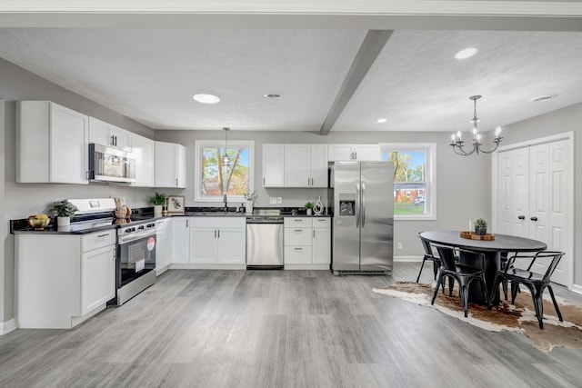 kitchen with white cabinetry, appliances with stainless steel finishes, a notable chandelier, pendant lighting, and beamed ceiling