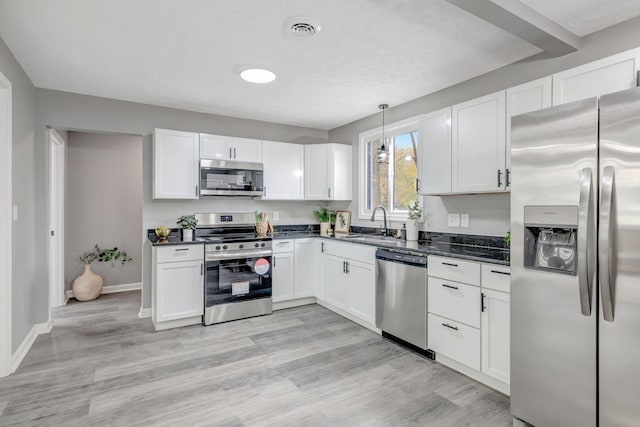 kitchen featuring stainless steel appliances, sink, white cabinetry, and decorative light fixtures