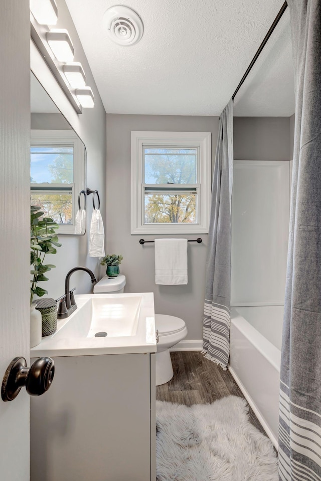 full bathroom with toilet, hardwood / wood-style floors, shower / bath combo with shower curtain, a textured ceiling, and vanity