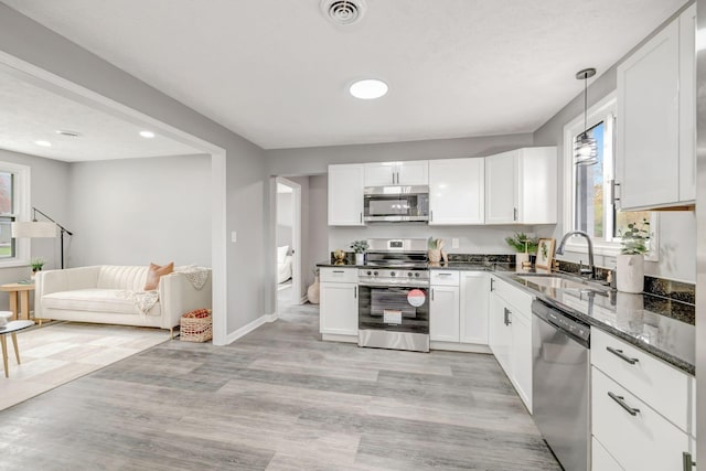 kitchen with white cabinetry, light hardwood / wood-style floors, stainless steel appliances, pendant lighting, and sink