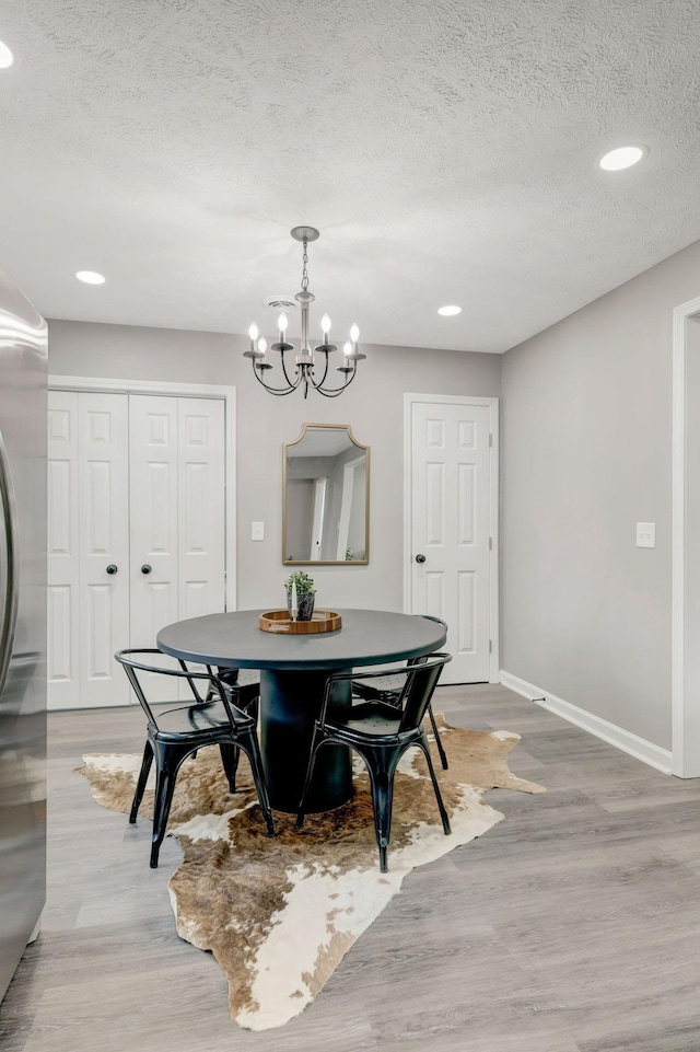 dining space with an inviting chandelier, a textured ceiling, and light hardwood / wood-style flooring