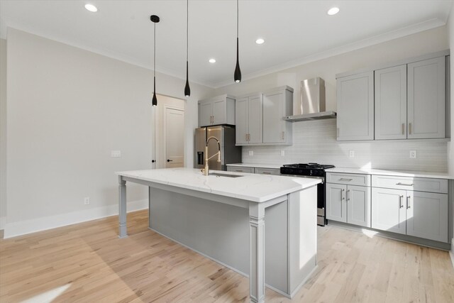 kitchen with crown molding, an island with sink, gray cabinets, stainless steel appliances, and wall chimney exhaust hood