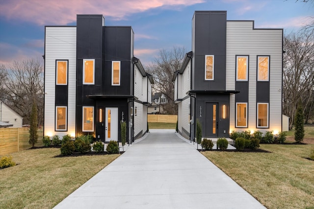 modern home with concrete driveway, a front lawn, and fence