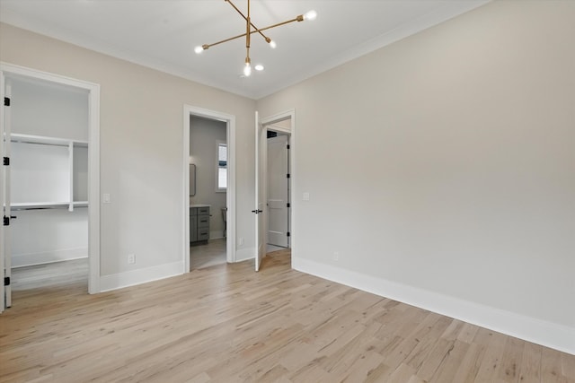 unfurnished bedroom featuring a walk in closet, baseboards, a notable chandelier, and light wood finished floors