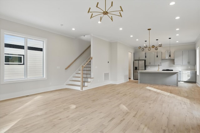 unfurnished living room featuring stairway, visible vents, baseboards, light wood-style flooring, and crown molding