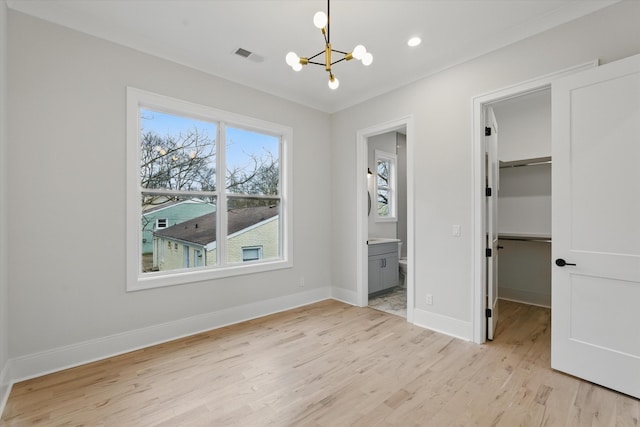 unfurnished bedroom with light wood-style flooring, a spacious closet, visible vents, and a chandelier