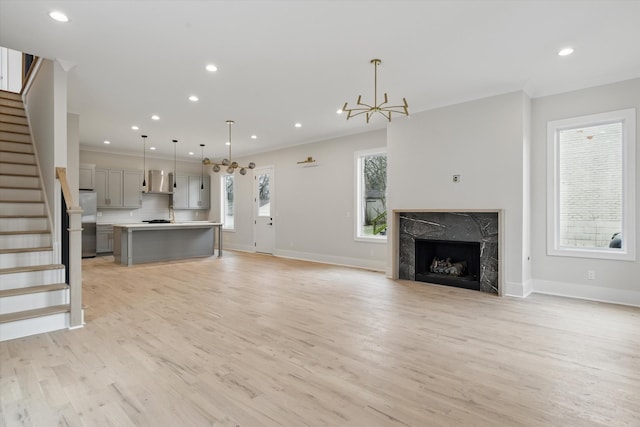 unfurnished living room featuring recessed lighting, a fireplace, stairs, light wood-type flooring, and a chandelier