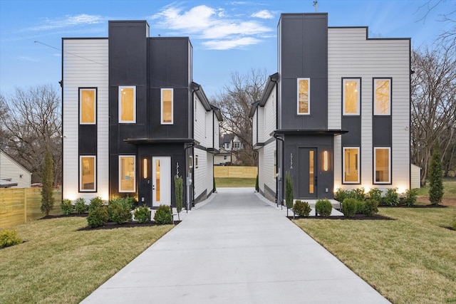 contemporary home featuring concrete driveway, a front lawn, and fence