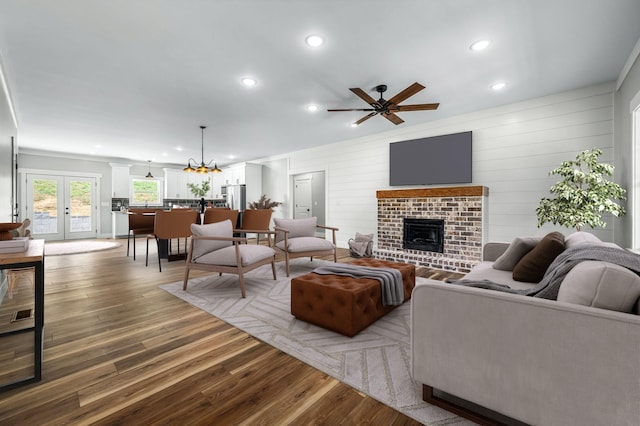 living room featuring french doors, a brick fireplace, ceiling fan with notable chandelier, and wood-type flooring