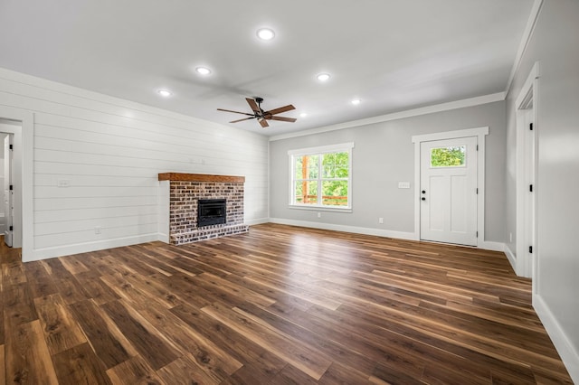 unfurnished living room with wooden walls, ceiling fan, dark hardwood / wood-style floors, a fireplace, and crown molding