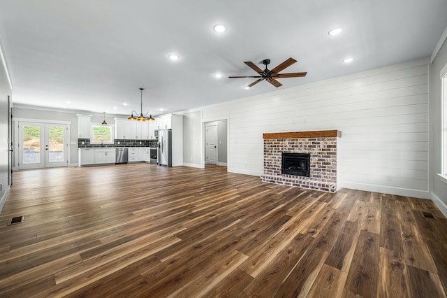 unfurnished living room with dark hardwood / wood-style flooring, sink, ceiling fan with notable chandelier, and a brick fireplace