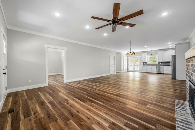 unfurnished living room featuring a brick fireplace, sink, dark wood-type flooring, ornamental molding, and ceiling fan with notable chandelier