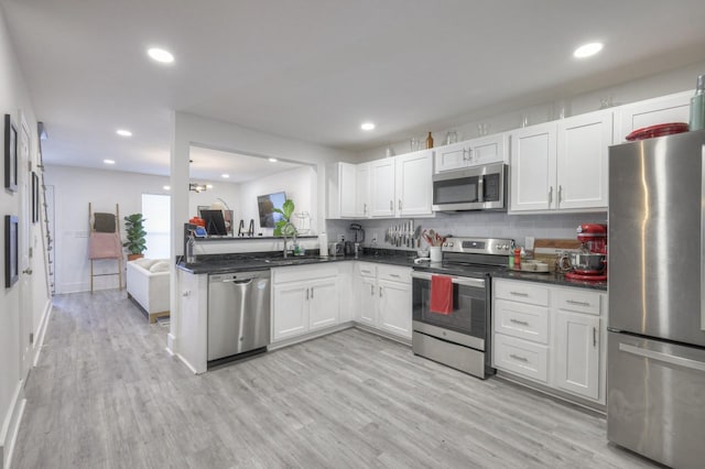 kitchen with white cabinetry, stainless steel appliances, decorative backsplash, sink, and light hardwood / wood-style flooring