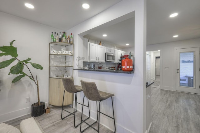 kitchen featuring backsplash, light hardwood / wood-style floors, kitchen peninsula, white cabinetry, and a kitchen breakfast bar