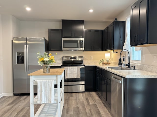 kitchen with appliances with stainless steel finishes, light countertops, a sink, and light wood-style flooring