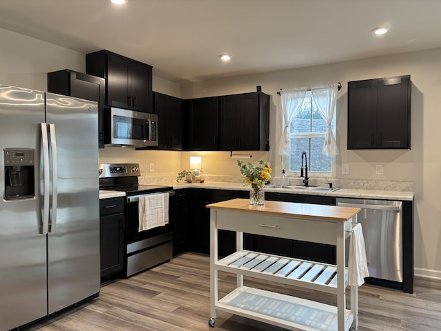 kitchen with stainless steel appliances, light wood finished floors, a sink, and dark cabinets